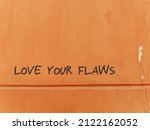 Small photo of Old grunge orange wall with red text LOVE YOUR FLAWS, concept of positive self talk, learning self love and boost confidence, appreciate and accept our own flaws