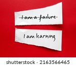 Small photo of Torn paper stick on red background with handwriting I AM A FAILURE, corrected to I AM LEARNING, to overcome negative self talk, replace with positive thoughts, with respect and self worth