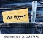 Small photo of Note in jean pocket with handwritten text JOB HOPPER, means person who works briefly in one position after another rather than staying long term in organization