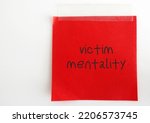 Small photo of Red stick note paper with handwriting VICTIM MENTALITY - personality trait of person who believe themselves a victim as if the world is against them or bad things keep happening