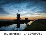 Noctilucent clouds (NLCs) or polar mesospheric clouds, looking north at midsummer night. Classic dutch scene with a canal and windmill silhouet against the evening sky.