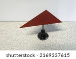 Small photo of Physics experiment where a red triangular metal plate is balancing on a needle. The center of gravity of the triangle is placed exactly at the tip of the needle.