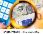 Small photo of A person with a magnifying glass looking for money. Dollar and Euro together being observed in a photo with a blurred background. International business and world economy concepts.