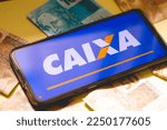Small photo of Brasilia, Federal District - Brazil. January, 16, 2023. A cell phone with the Federal Savings Bank ( Caixa Economica Federal ) logo and Brazilian Real banknotes. Yellow paper background.