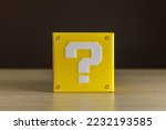 Small photo of Indoor still-life photo of a little yellow box with a big white question mark printed on each face. It recalls a graphic element of a famous platform video game.