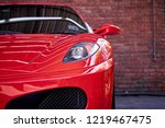 Close up of headlight detail of modern luxury sportscar with reflection on red paint after wash & wax. Front view of supercar with brick wall. Concept of car detailing and paint protection background.