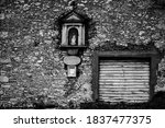 black and white photo of a house facade with closed vintage shutter and capital with Madonna and child
