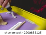 Small photo of Hands of tattoo artist putting white ink in plastic container in a table with new needle and stick with vaseline