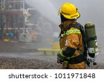 View of a fire fighter with compressed air tank. Visible water mist in the background.