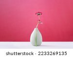 Small photo of Two daisy spring flowers near a tiny green vase on table. Misplaced eccentric. Fragile. assumptions. Unordinary. Viva magenta background with copy space. Blooming flowers. Greeting card. Border banner