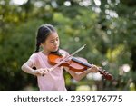 Small photo of Cute Asian little girl playing the violin in the park, education music concept