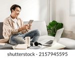 Small photo of Happy smiling Asian student sits and relaxes on a couch using modern tablet browsing unlimited wireless internet, positive young man freelancer working uses wifi at a home apartment, technology idea.