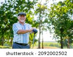 Small photo of Portrait of Smiling Asian senior man golfer holding golf club standing on golf course in summer sunny day. Healthy elderly male enjoy outdoor lifestyle activity sport golfing at golf country club.