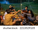 Group of Asian man and woman friends enjoy and fun outdoor lifestyle celebrating holiday event with toasting beer bottle and have dinner together near the tent while camping on summer travel vacation.