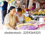 Happy Asian family mother and daughter choosing and buying fresh flower together at florist shop street market for flower vase arrangement celebrating holiday event on summer vacation at home