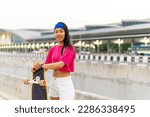 Portrait of Asian woman holding longboard skate during skating at park on summer vacation. Attractive girl have fun urban active lifestyle practicing outdoor sport skateboarding in the city at sunset.