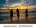 Group of Young Asian woman friends playing sparklers firework together at tropical island beach in summer night. Attractive girl enjoy and fun outdoor lifestyle beach party on holiday travel vacation.