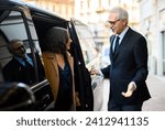 Senior businessman is engaging in a friendly conversation with a female assistant while entering a luxurious limousine