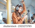 Small photo of Happy young Asian woman passenger listening music via smart mobile phone in a train, Smile female wearing wireless headphones while moving in the tram, lifestyle, transportation.