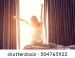 Woman standing near the window while stretching near bed after waking up with sunrise at morning, back view