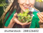 Portrait of attractive caucasian smiling woman eating salad, focus on hand and fork. soft, backlight