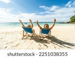 Two happy people having fun on the beach, sitting on blue sunbed with hands raised up, spending leisure time together. Summer holidays concept. Tourism. Travelers.