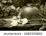 Old, holey, rusty German military helmet of the Second World War with white tulips on the stone, toning