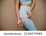 Small photo of Cropped view of slim woman measuring bdr with tape measure at home, close up. A European woman checks the result of a weight loss diet or liposuction indoors. Healthy lifestyle.