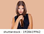 Beauty Portrait Young Woman holding her long natural brown Hair with her hands. Makeup. Brunette model with long hair posing over Beige background. Girl looking at camera. Eye makeup, peach lips   