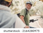 Two happy old mature people enjoying and riding bikes together to be fit and healthy outdoors. Active seniors having fun training in nature. Portrait of one old man smiling in a bike trip with wife