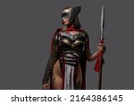 Small photo of Studio shot of wild female warrior from past with painted face holding spear isolated on grey background.