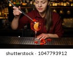Woman barman decorating a glass of fresh and tasty Aperol syringe cocktail with red rose petals
