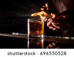 The bartender makes flame over a cocktail with orange peel close up
