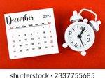 December 2023 Monthly calendar year with alarm clock on red background.