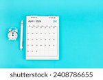 April 2024, Monthly desk calendar for 2024 year and pen with alarm clock on blue color background.