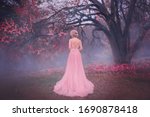 Small photo of Mysterious silhouette princess. young blonde woman queen turned away. backdrop autumn nature mystic blue fog pink full bloom fairy tree black trunk. spring pink long elegant vintage dress bare back
