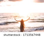 Small photo of happy woman stands seashore turned away hand raised to heaven sky sun light. Lady girl enjoy sunny sunset sea waves. Concept hope divine pray freedom. Brunette long hair fluttering fly wind. Georgia