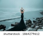 Small photo of fantasy woman. young adult girl Snow Queen walks on frozen frost lake, river. Winter nature, ice cold covered water. Lady turned away, back train. Black dress mermaid Silhoette. Fashion model posing