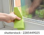Woman hand wipes off water condensation in room with high humidity level. Home moisture with water condensation on the window glass.