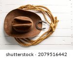 Small photo of Classic brown cowboy hat lasso and horseshoe wild west still life on rough white wooden table