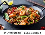 Stir fry noodles with vegetables and shrimps in black iron pan. Slate background. Close up.