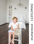 Small photo of The little tetchy girl sits on a chair in the bedroom. Vertical view