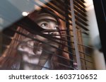 Asian woman looking through window blinds spying on neighbours - Young lonely millennial woman peeping through glass observing gossip and action outdoors - introvert, privacy and intrusive concepts