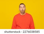Small photo of Hispanic man with a beard in a red sweatshirt with his eyes wide with emotion, his mouth is open in surprise generated by something unheard of. Isolated on yellow background.
