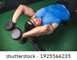 Small photo of A fit asian man does a set of lying dumbbell tricep extensions. Working out Triceps and arms at the gym.