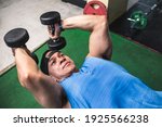 Small photo of A muscular and buff asian man does a set of lying dumbbell tricep extensions. Working out Triceps and arms at the gym.