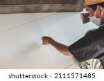 Small photo of A handy man applies grout to fill the gaps of white porcelain floor tiles at the living room. Home renovation or finishing works.