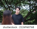 Small photo of A young handsome man looking to a young woman somewhere in the park. Expressing interest, infatuation and love.