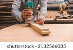 Small photo of A carpenter uses a wood trimmer to chamfer to edge of a table leg. Compact Wood Palm Router Tool. At a furniture making workshop.