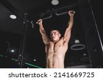 Small photo of An athletic man hangs on a pull up bar. Training lats and back. Shirtless revealing his brawny and sinewy torso.
